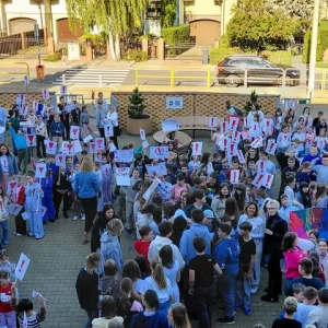 Uczniowie zgromadzeni przed szkołą trzymają plakaty z czerwonymi wykrzyknikami.
