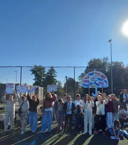 Grupa uczniów na boisku prezentuje transparenty, w tym plakat w kształcie parasola.